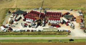 A Weatherford well completion site in Canadian County, Okla., in the Woodford Shale is surrounded by close to 30 frac pumps, the number required to pump 100 bbl/min at over 10,000 psi surface treating pressure. The black water tanks (rear left) hold water that is being pulled out by the adjacent truck and transported to the frac pumps.